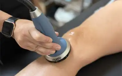 Shockwave therapy treatment being applied to a patient's leg with a handheld device during a chiropractic rehabilitation session in Plano, TX.