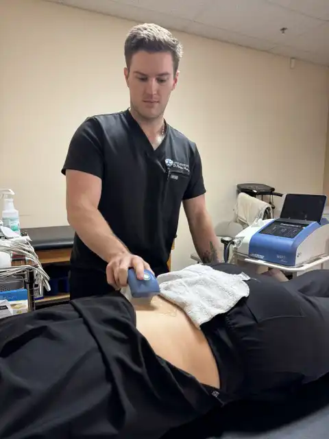 Healthcare provider performing shockwave therapy on a patient’s lower back using a handheld treatment device while the patient lies on a chiropractic treatment table.